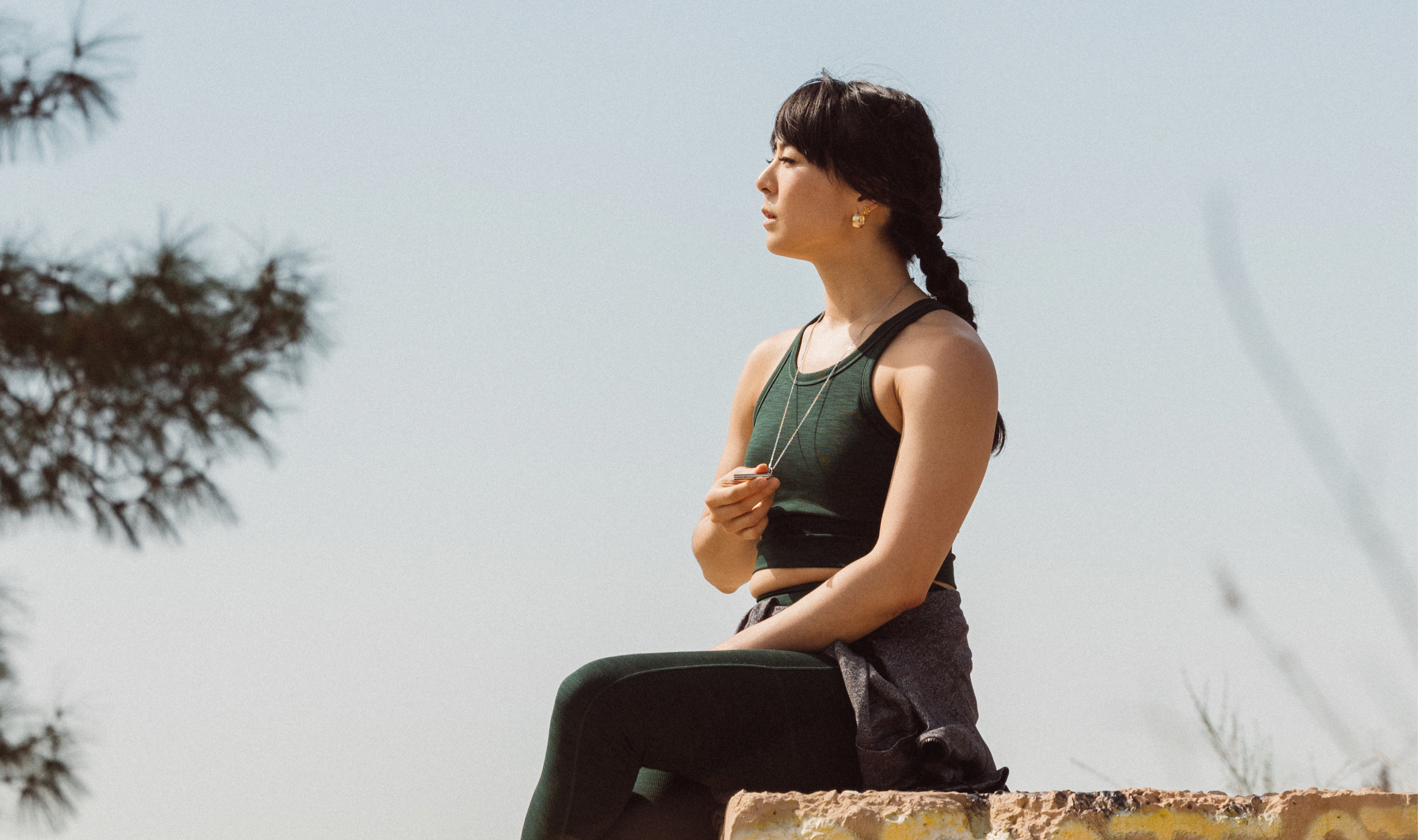 Woman holding the Komuso Classic Shift breathing necklace while looking into the distance, pausing for a micro-calming breathing moment.